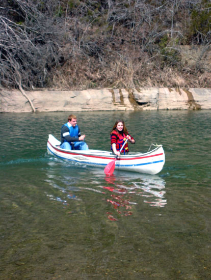 White man and woman navigating a river in a striped canoe