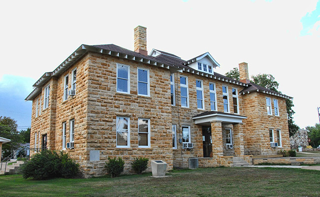Multistory stone building with covered porch on grass