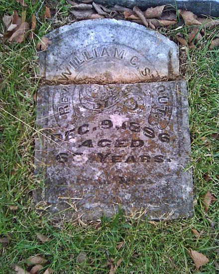 Broken stone marker laying in the grass "Rev. William C. Stout"