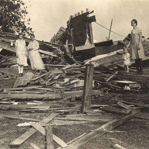 Three white women and child standing in debris of destroyed house