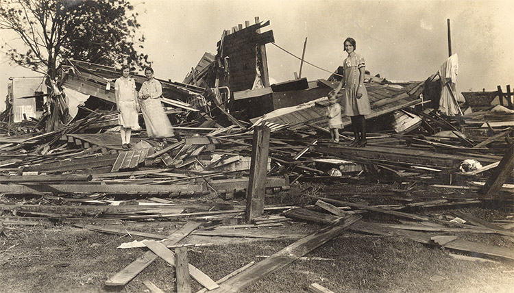 Three white women and child standing in debris of destroyed house