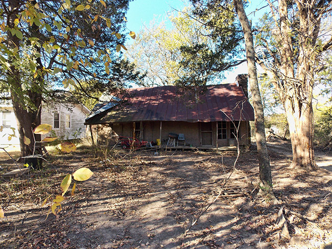 Single-story house with covered porch and rusted metal roof in forested area
