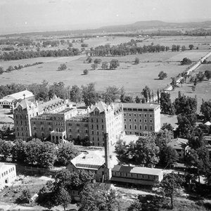 Multistory abbey building and campus buildings with water tower and countryside in the background