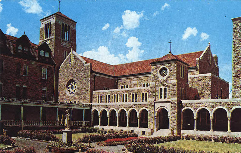Multistory building with bell tower stained glass windows covered walk ways and clock tower surrounding courtyard with flowers and statue