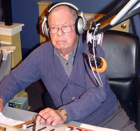 Old white man with glasses and headphones sitting in radio booth
