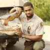 Young African-American man kneeling in uniform with alligator in truck bed