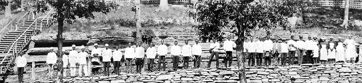African-American men in uniforms standing in line with staircase and rock wall behind them