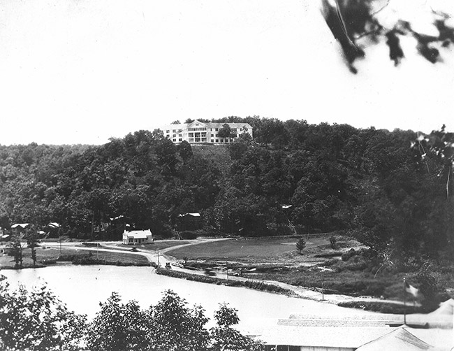 Three-story hotel on a hill with house and pond below it
