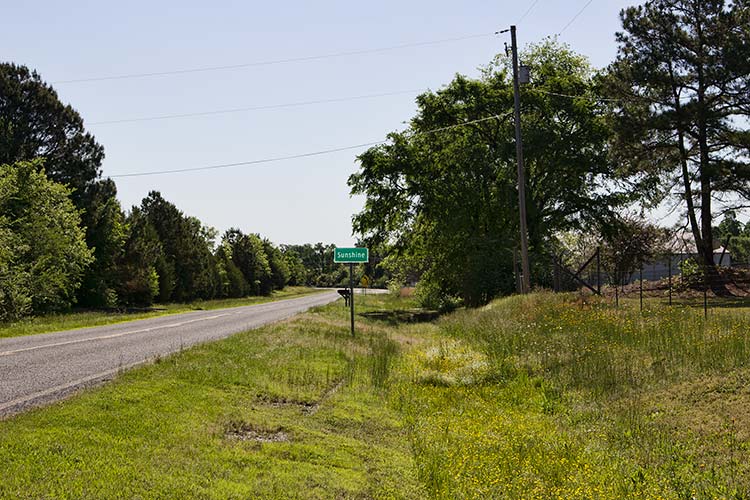 Rural road with green "Sunshine" sign on its right side