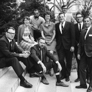 Group of white men and two white women smiling on steps outdoors