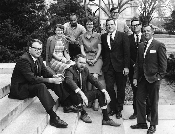 Group of white men and two white women smiling on steps outdoors