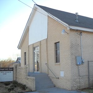 buff brick church building with sign and steps up to the entrance