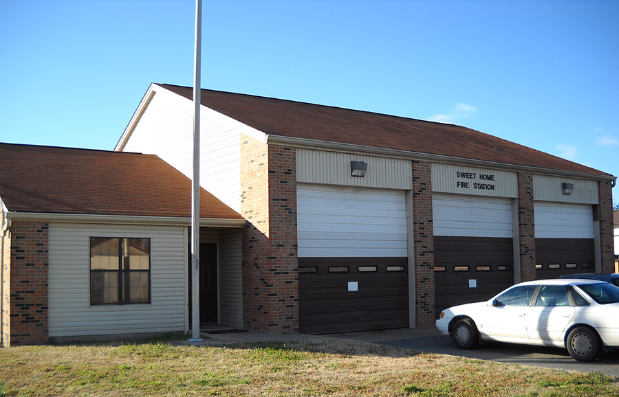 Cars parked at brick fire department building with three garage bay doors