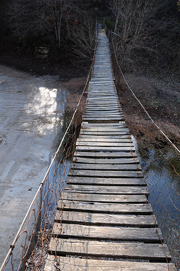 Looking across wooden bridge suspended over creek