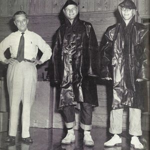 Older white man in shirt and tie with two young white men in rain coats