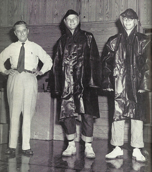 Older white man in shirt and tie with two young white men in rain coats