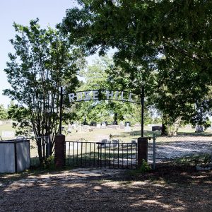 "Rose Hill" cemetery gates with iron arch sign and brick columns under trees with fence