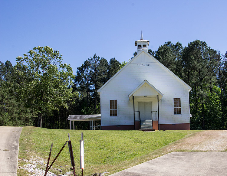 Single-story church building with A-frame roof with cupola and covered entrance on grass
