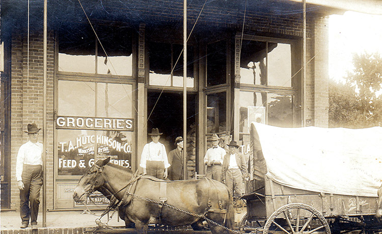 White men outside storefront with horse and covered wagon