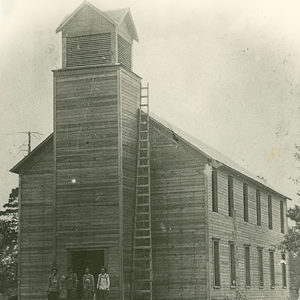 Four white men standing on steps of large wooden church building with bell tower