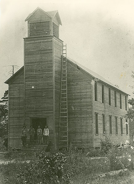 Four white men standing on steps of large wooden church building with bell tower