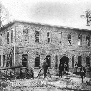 Group of white men and women standing outside of two-story brick building