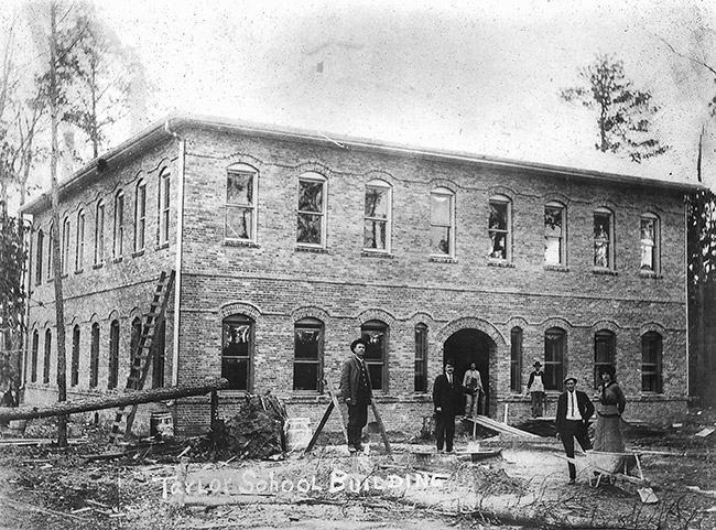 Group of white men and women standing outside of two-story brick building
