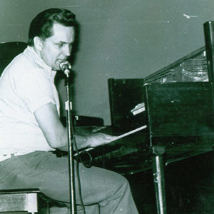 Young white man singing into microphone and playing piano