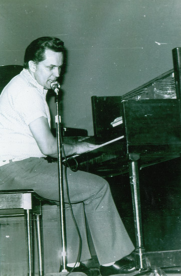 Young white man singing into microphone and playing piano