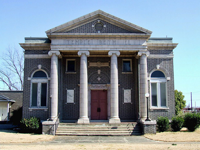 Multistory brick building with covered porch supported by four columns and arched windows with "Temple Beth El" engraved on the front