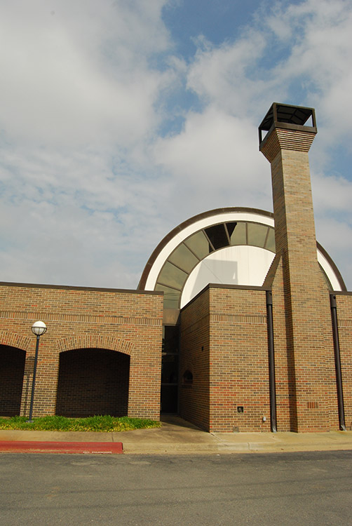 Single-story brick building with hemispherical dome chimney and arched walkway on parking lot