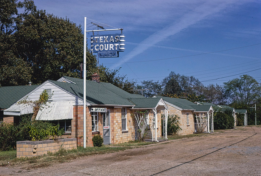 Row of single-story brick buildings with "Texas Court" hanging sign in foreground