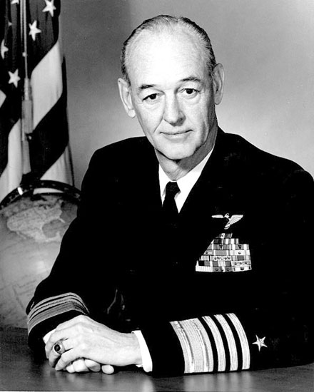 Older white man with in military uniform with American flag and a globe in the background