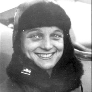 White woman wearing a furry jacket with a flag pin smiling at the camera