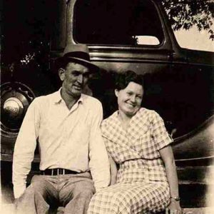 White man in hat and woman sitting on wall with Ford truck behind them