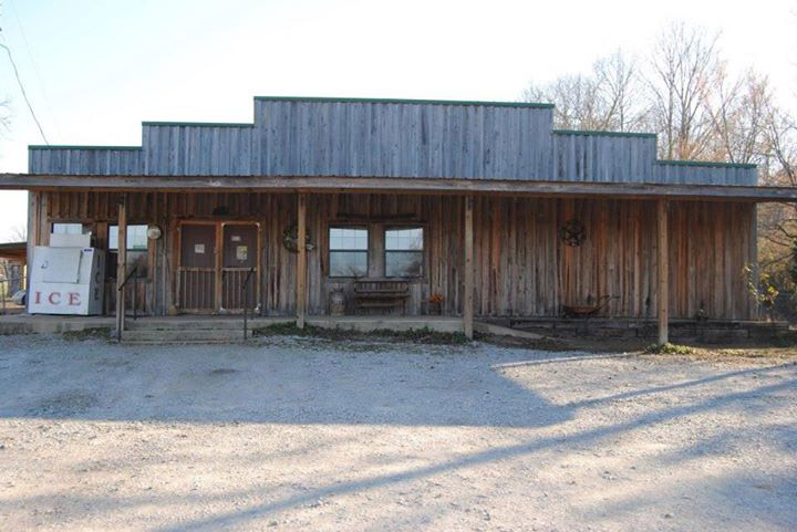 Single-story storefront with covered porch and ice machine on gravel parking lot