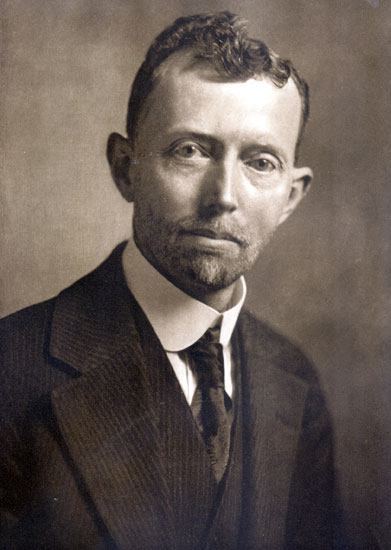 White man with curly hair and beard in suit and tie