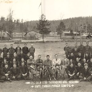 Group of white men in uniform with camp buildings behind them