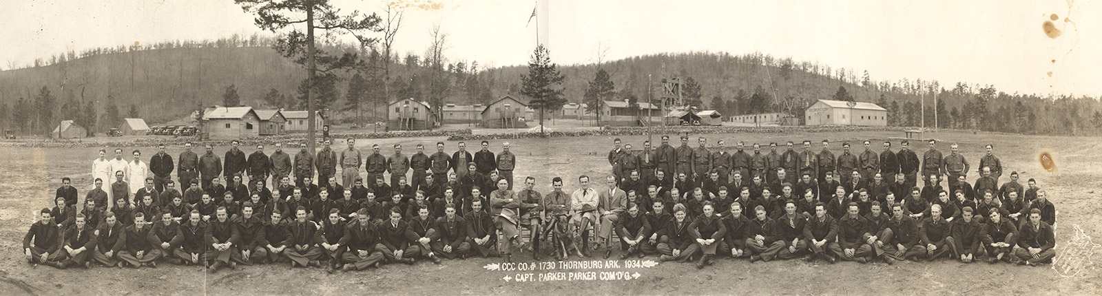 Group of white men in uniform with camp buildings behind them