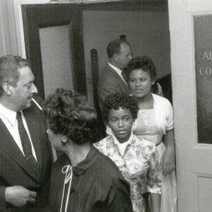 White men and African-American man in suits outside courtroom with African-American woman and girls