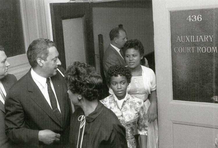 White men and African-American man in suits outside courtroom with African-American woman and girls