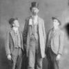 Tall white man in top hat and suit standing between two white men with hats in suits