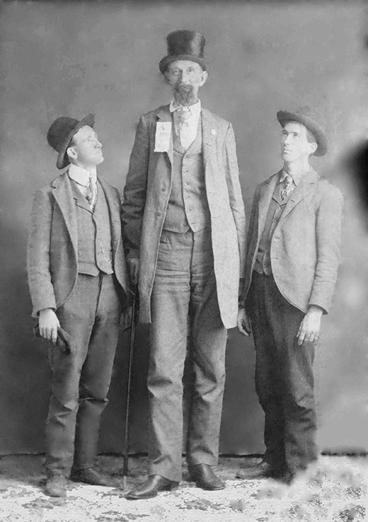 Tall white man in top hat and suit standing between two white men with hats in suits