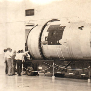 Group of men examining large cylindrical object.