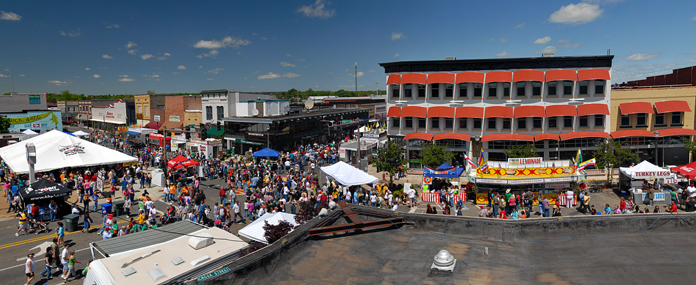 Crowded town square with tents and food stands in front of multistory buildings