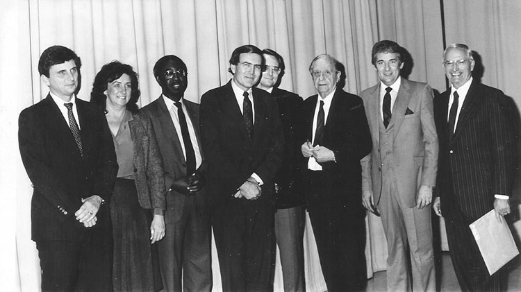 African-American man in suit and tie standing with white men in suits and ties and white woman in dress