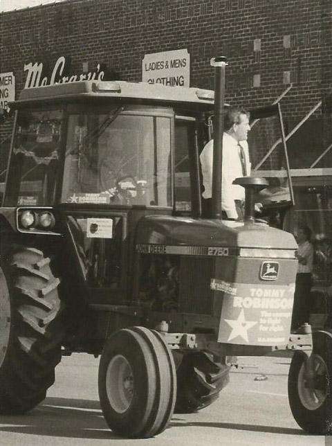 White man on tractor in parade with brick building in the background