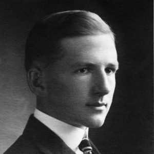 Portrait of young dark-eyed white man with a close-lipped smile and hair combed smooth in suit jacket and tie