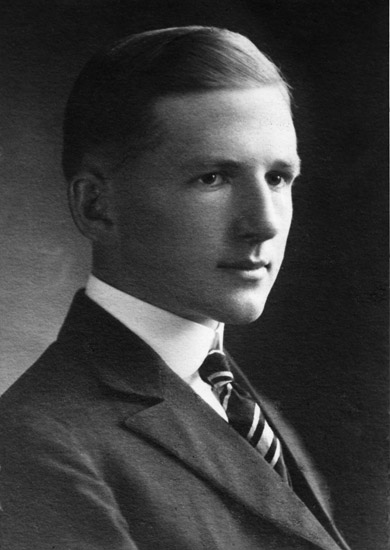 Portrait of young dark-eyed white man with a close-lipped smile and hair combed smooth in suit jacket and tie