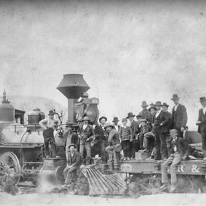 Group of white men in hats and suits gathered around a steam locomotive